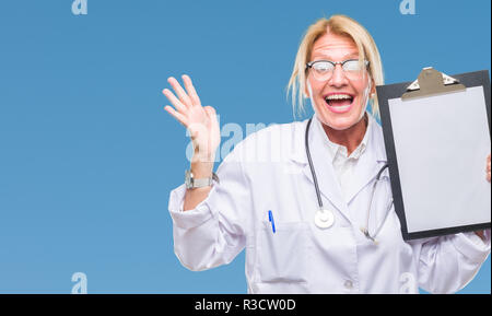 L'âge moyen médecin blonde woman holding clipboard sur fond isolé très heureux et excité, lauréat des cris de victoire célèbre expression Banque D'Images