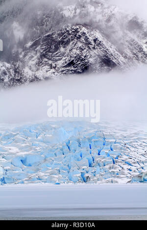 USA, Alaska. Le visage de l'Mendenhall Glacier émerge des nuages qu'il rencontre la lac Mendenhall congelé. Banque D'Images