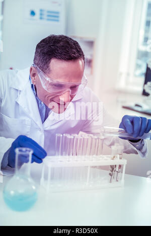 Être attentif. Genre brunette homme gardant sourire sur son visage tout en regardant les tubes à essai Banque D'Images