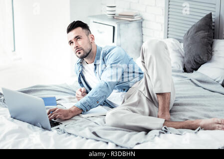 Permettez-moi de penser. Homme barbu concentré traversant les jambes tout en se penchant sur le lit et d'être en profonde réflexion Banque D'Images