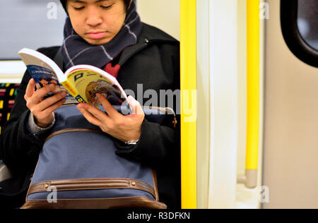 Jeune homme japonais Hentai la lecture d'un roman graphique sur un train de tube, Londres, Angleterre, Royaume-Uni. Banque D'Images