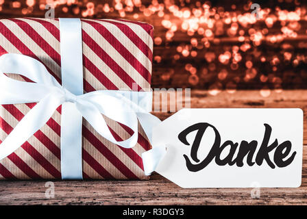Un cadeau de Noël avec étiquette avec calligraphie allemand Danke veut dire merci. Cadeau avec ruban rouge et blanc avec du papier d'emballage. Fond de bois avec Bok Banque D'Images