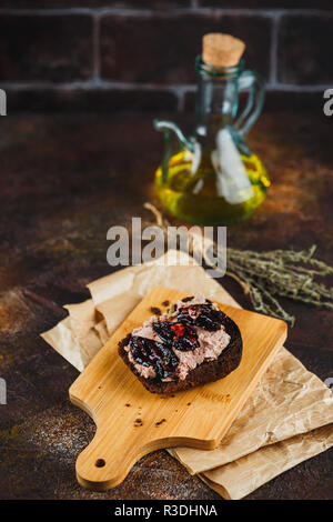 Sandwich avec patee canard et les prunes séchées sur une planche à découper en bois, de l'huile d'olive, sel, poivre, ail et branches de thym sur fond sombre Banque D'Images