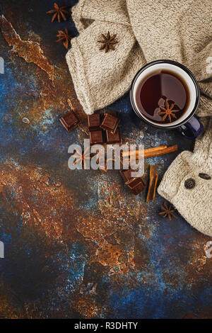 Émaillé bleu tasse de thé, des bâtons de cannelle, d'anis étoile, morceaux de chocolat noir et pull en laine chaud sur un fond sombre. Vue d'en haut. L'espace pour le texte. Banque D'Images