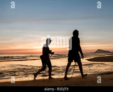Mature couple walking avec poteaux, marche nordique, sur la plage au lever du soleil en Espagne. Banque D'Images