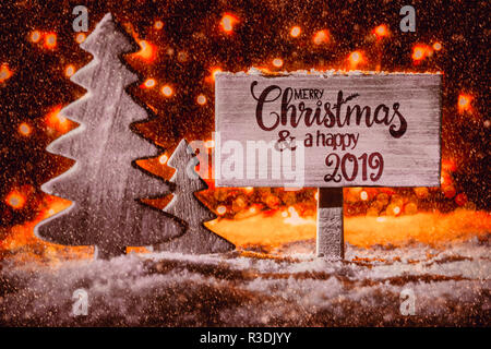 Panneau en bois avec calligraphie anglaise Joyeux Noël et une Bonne 2019. Arbre de Noël sur la neige et Fairy Lights en arrière-plan. Pleins feux rouge Banque D'Images