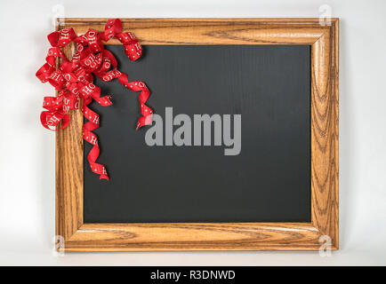 Ruban rouge Noël Curly sur retro noir ardoise avec cadre en bois Banque D'Images