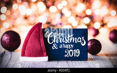 La plaque avec la calligraphie anglaise Joyeux Noël et une Bonne 2019. Et mousseux lumières fond étincelant. Décoration de Noël Boules violet comme un Banque D'Images