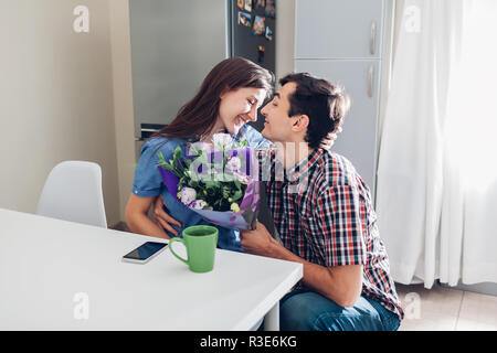 Jeune homme gifting bouquet de fleurs à sa petite amie dans la cuisine. Heureux couple hugging. Surprise romantique à la maison Banque D'Images