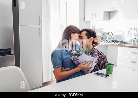 Jeune homme gifting bouquet de fleurs à sa petite amie dans la cuisine. Heureux couple hugging. Surprise romantique à la maison Banque D'Images