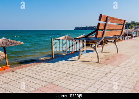 Banc en bois est placé sur l'allée carrelée derrière, mais au-dessus de la plage publique avec transats près de la côte. Banque D'Images