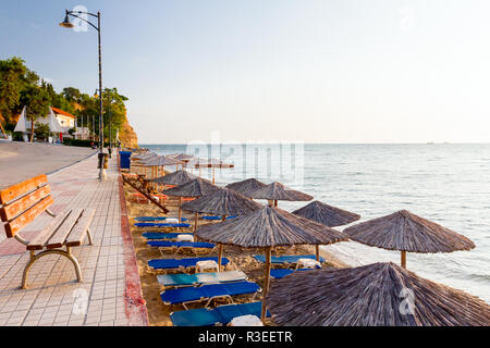 Banc en bois est placé sur l'allée carrelée derrière, mais au-dessus de la plage publique avec des parasols en chaume, parasols et transats près de la côte. Banque D'Images