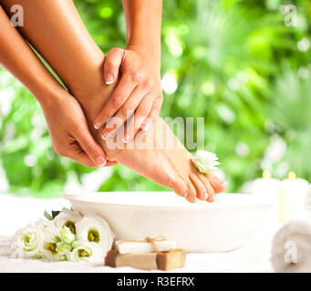 Les pieds et les mains avec spa bol, serviette, savon et de fleurs sur sol blanc et vert tropical leaves background Banque D'Images