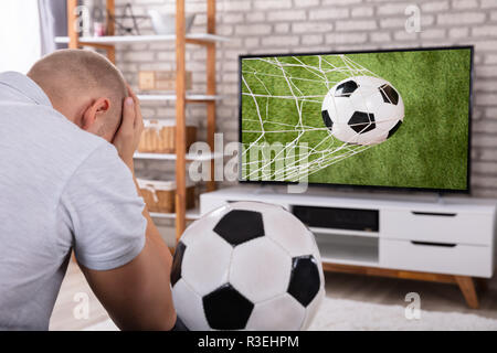 Triste homme assis près de la télévision montrant Match de football Banque D'Images