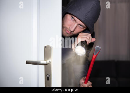 Voleur avec lampe et Crowbar Peeking de porte Banque D'Images