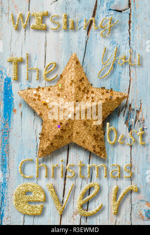 Carte de Noël. Voeux de Noël Simple avec de belles lettres en message de golden glitter et une étoile sur fond rustique en bois bleu, vertical de l'image. Banque D'Images