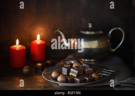 Bonbons de chocolat de Noël, deux bougies rouges et une teapott d'argent sur une table rustique en bois foncé, fond, moody mise au point sélectionné, étroite profondeur de fiel Banque D'Images