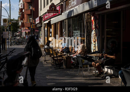 Les gens à l'extérieur de détente au soleil à la terrasse d'un café à Neukolln, Berlin, Allemagne. Banque D'Images