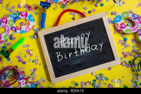 Fête d'anniversaire. Joyeux anniversaire texte sur un tableau noir, confetti et serpentins sur fond jaune lumineux, vue du dessus Banque D'Images