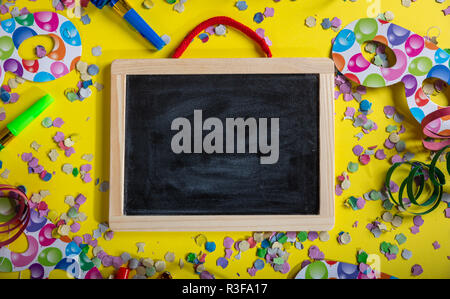 Carnaval ou fête d'anniversaire. Blank blackboard, confetti et serpentins sur fond jaune lumineux, vue du dessus, copy space Banque D'Images