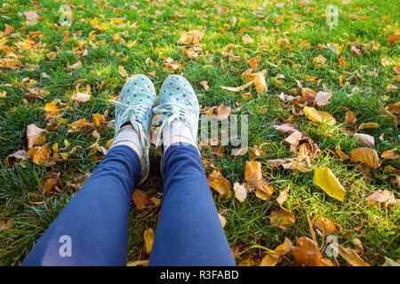 Fille dans le parc de l'automne. sneakers sur fond d'herbe et feuilles jaunes Banque D'Images