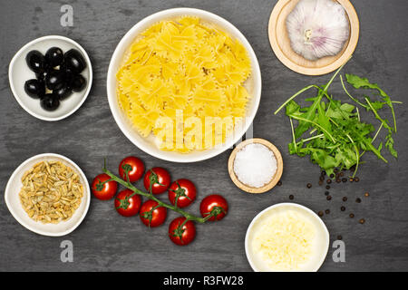 Étape par étape la recette farfalle avec ingrédients feuilles de roquette sur flatlay pierre gris Banque D'Images