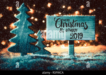 Panneau en bois avec calligraphie anglaise Joyeux Noël et une Bonne 2019. Arbre de Noël sur la neige et Fairy Lights en arrière-plan. Spotlight bleu Banque D'Images