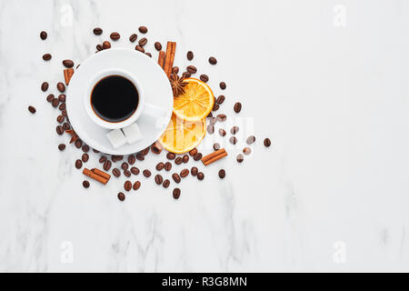Tasse de café avec des haricots, du chocolat, des oranges séchées, des bâtons de cannelle et anis sur fond de marbre blanc. Concept de café avec différentes épices. Haut Banque D'Images
