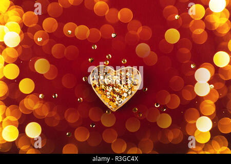 Boîte en forme de coeur avec des paillettes d'or sur fond rouge. Mise à plat de style. Concept de fête. Banque D'Images