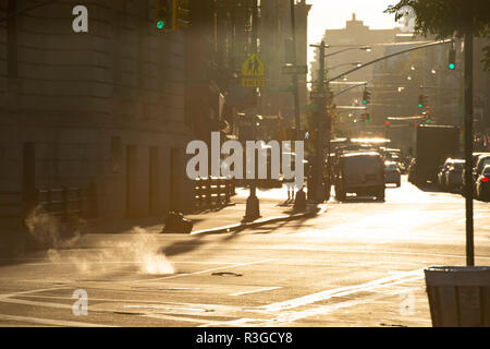 Beau lever de soleil dans les rues de Manhattan, avec un trou qui propulse la vapeur et voitures sur arrière-plan, New York, United States. Banque D'Images