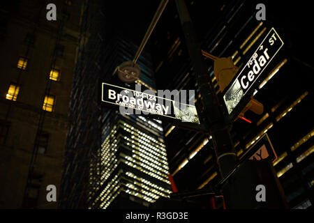 (Selective focus) rue Broadway, signer et Cedar St. signer éclairés la nuit à Manhattan, New York. Vapeur s'échappant de l'écoutille sur le côté droit. Banque D'Images