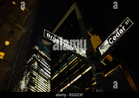 (Selective focus) rue Broadway, signer et Cedar St. signer éclairés la nuit à Manhattan, New York. Vapeur s'échappant de l'écoutille sur le côté droit. Banque D'Images