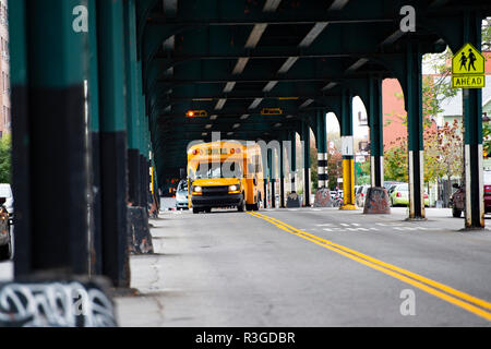 Un autobus scolaire est passé sous le pont de chemin de fer dans le Bronx, New York City, USA. Banque D'Images