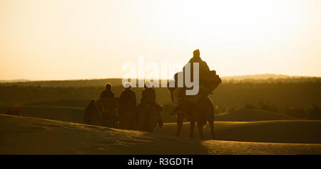 Certains touristes sur des chameaux traversant les dunes de sable dans le désert du Sahara au coucher du soleil - Maroc. Banque D'Images