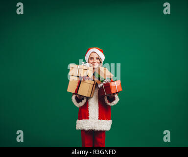 Girl dressed as santa holding christmas gifts debout sur un fond vert. Happy girl debout avec son cadeaux de Noël. Banque D'Images