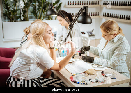 Blonde-haired woman qui souffle sur ses ongles assis dans le salon de manucure Banque D'Images