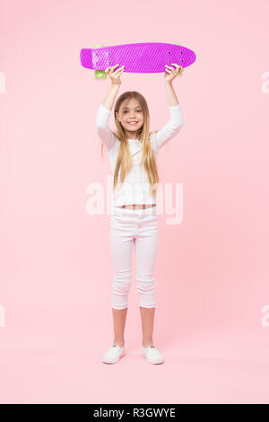 Boy holding skateboard violet au-dessus de sa tête. Champion de course de rue, enfance heureuse concept. Kid en cavalier blanc, jeans et baskets isolé sur p Banque D'Images