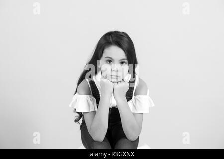 Enfant prop menton sur les mains sur fond bleu. Fille avec de longs cheveux de brunette en jeans dans l'ensemble. Beauté, mode, look, concept, copy space Banque D'Images