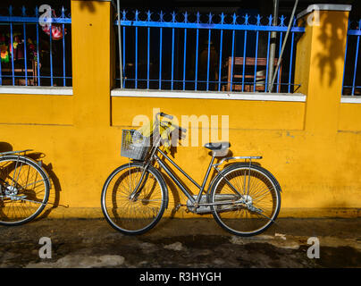 Les vélos garés près du mur jaune de la vieille maison sur la rue ensoleillée à Hoi An, au Vietnam. Banque D'Images