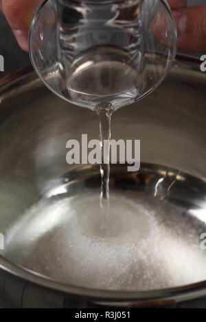 Verser de l'eau dans tas de sucre dans la casserole Banque D'Images