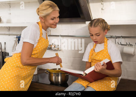 La cuisine grand-mère souriante et spaghetti à la petite-fille mignonne au livre de lecture dans la cuisine Banque D'Images