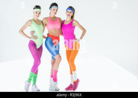 Les jeunes femmes attrayantes dans 80s style sportswear Standing together and smiling at camera sur gris Banque D'Images