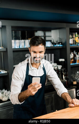 Barman debout avec smartphone et smiling in bar Banque D'Images