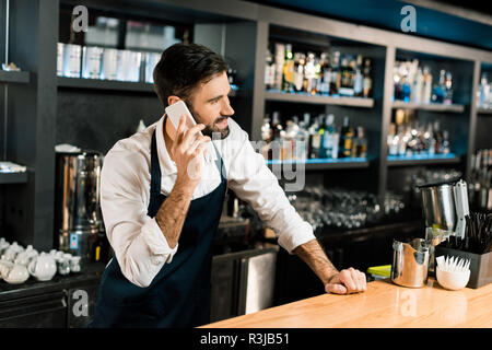 Barman parle sur smartphone et d'un tablier en bar Banque D'Images