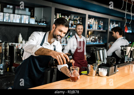 Smiling bartender pouring cocktail au comptoir de bois au verre Banque D'Images