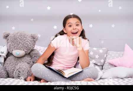 Deviner de son conte de fées. Petite fille s'asseoir lit avec ours lire livre. Kid se préparer à aller au lit. Temps agréable dans une chambre confortable. Ha long enfant fille Banque D'Images