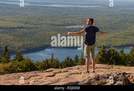 L'Acadia National Park, Maine--Septembre 21, 2016. Un homme se tient avec les bras tendus à la recherche sur le paysage d'un sommet de Cadillac Mountain dans le Budget principal Banque D'Images
