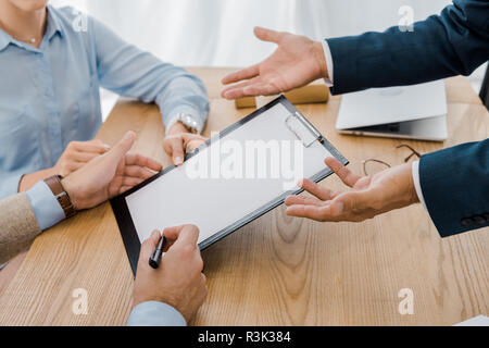 La signature de deux contrats au presse-papiers avec table en bois à l'agent d'assurance Banque D'Images