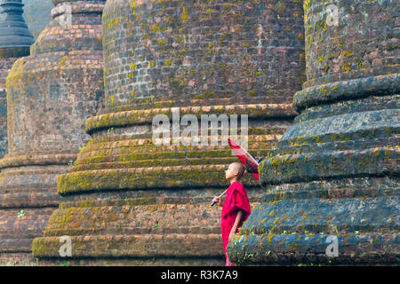 Monk holding parapluie rouge avec Andaw thein-Temple, Mrauk-U, l'État de Rakhine, au Myanmar Banque D'Images