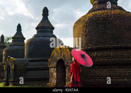 Monk holding parapluie rouge avec Andaw thein-Temple, Mrauk-U, l'État de Rakhine, au Myanmar Banque D'Images